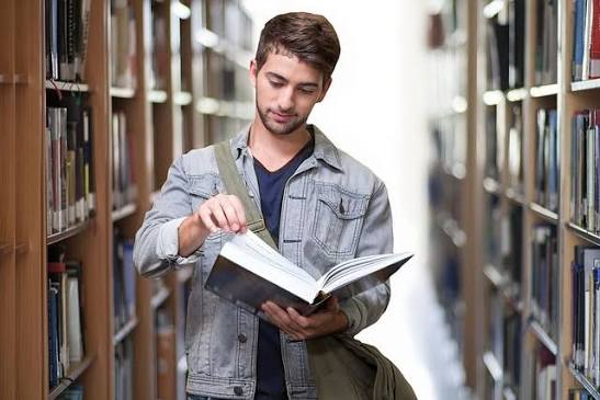 Student reading a book between library shelves