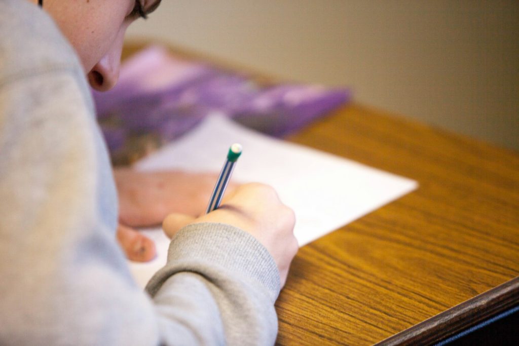 Student writing answers on a test paper at a desk